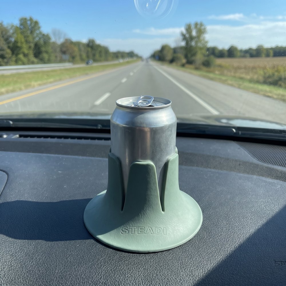 A can standing in a sage Steadi on a truck dashboard, road and sky through the windscreen.